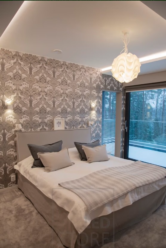 A modern room with stylish patterned wallpaper, a large bed with soft bedding, and high-quality LED lighting from LedStore.fi create the perfect atmosphere. The window offers a view of a snowy landscape, enhancing the cozy and peaceful ambiance. - LedStore In this bedroom, XL-Cubic wall lights are installed on the wall, along with LED strips in the light cove to create ambiance. The ceiling light adds a decorative touch and provides extra illumination to the room.
