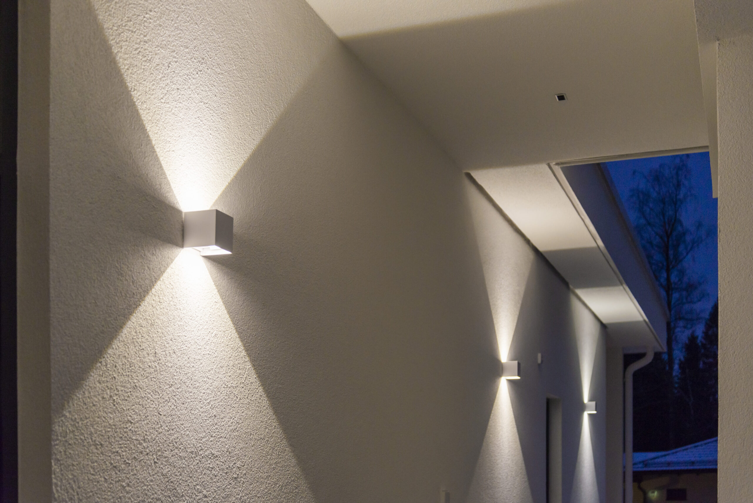 Cube-shaped white LED wall lights illuminate both upward and downward, creating a sharp light pattern on the wall.