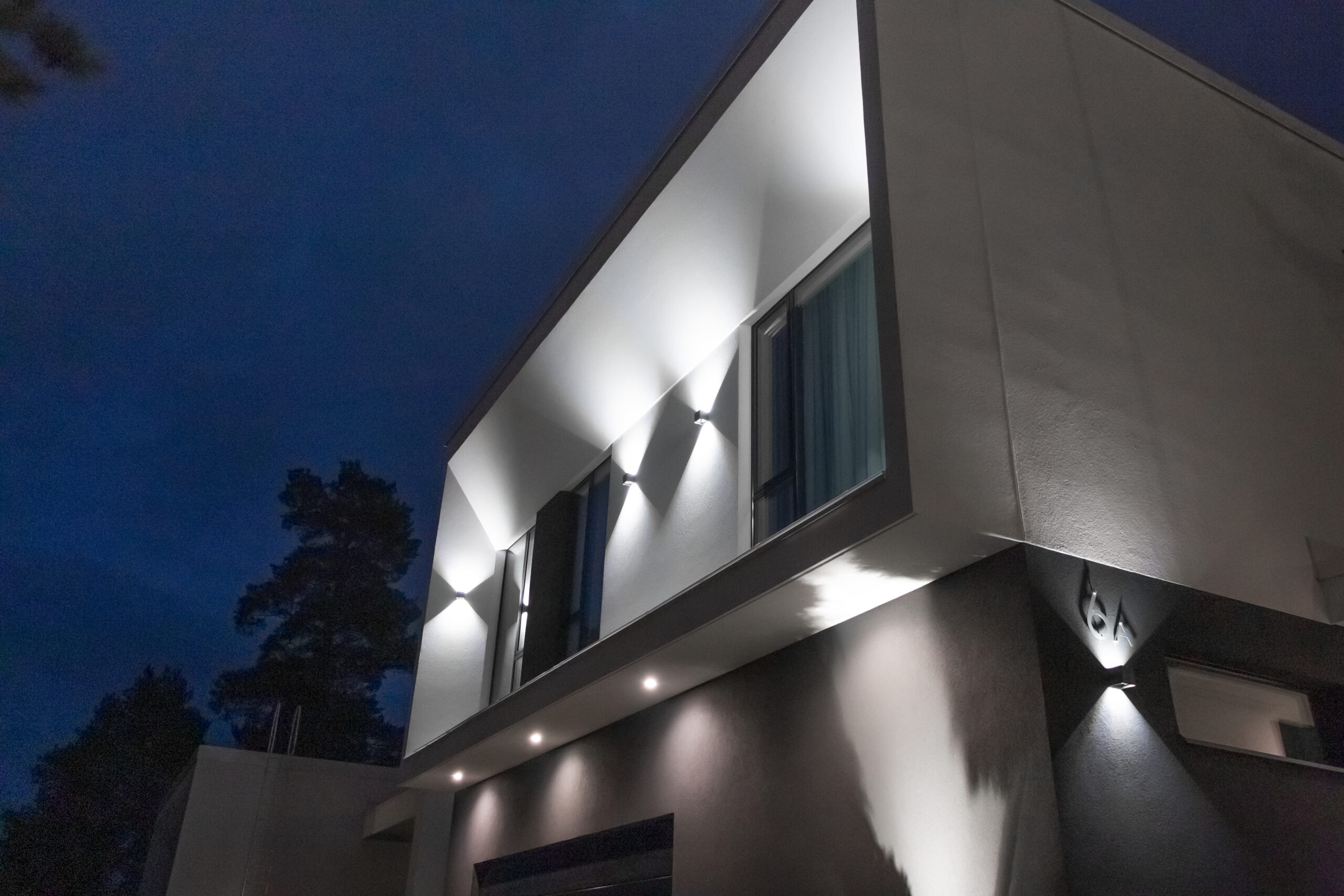 The facade of the house illuminated with wall lights and spotlights. 