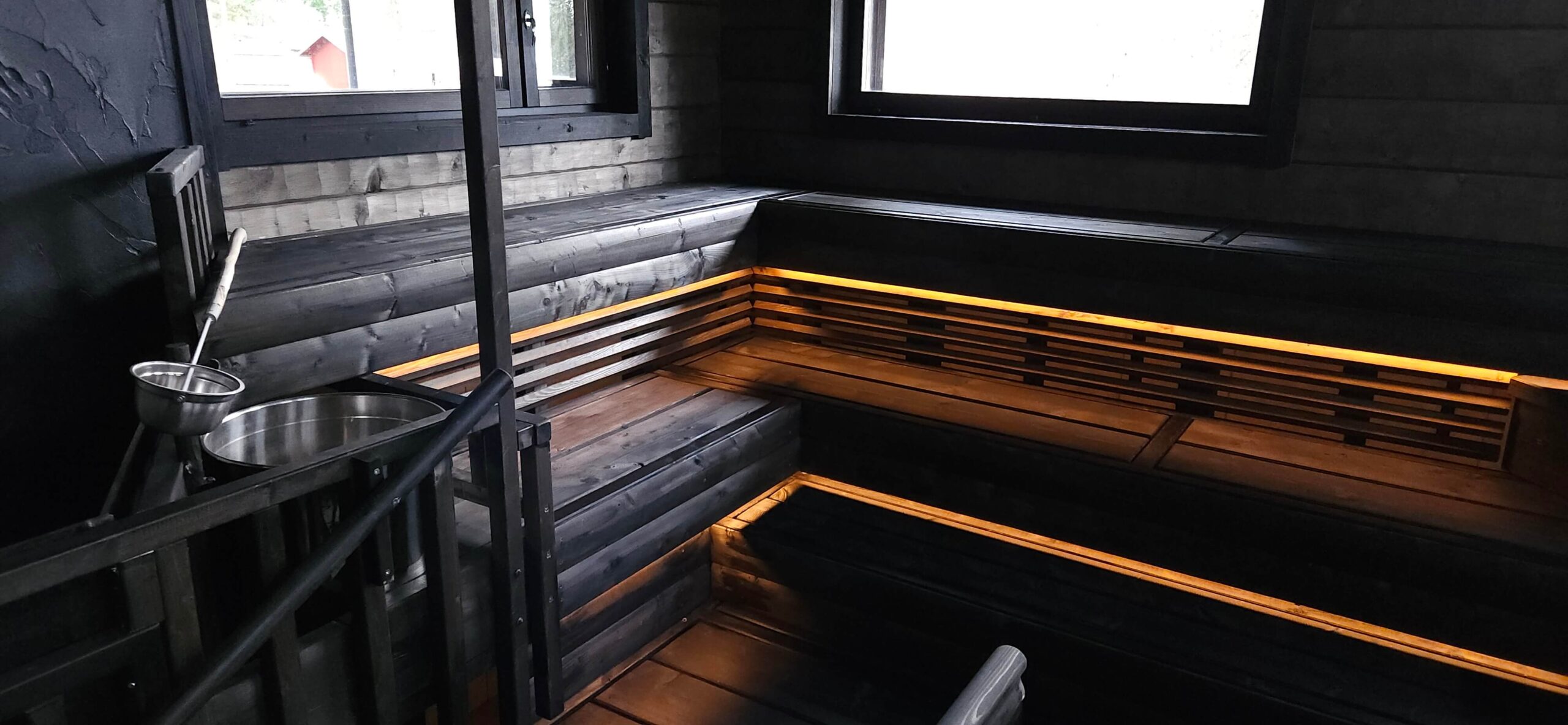 at the bottom of the dark wood sauna seat, warm yellowish LED strip lights installed to light downwards